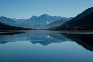 Mountain lake reflecting snow-capped peaks under blue sky